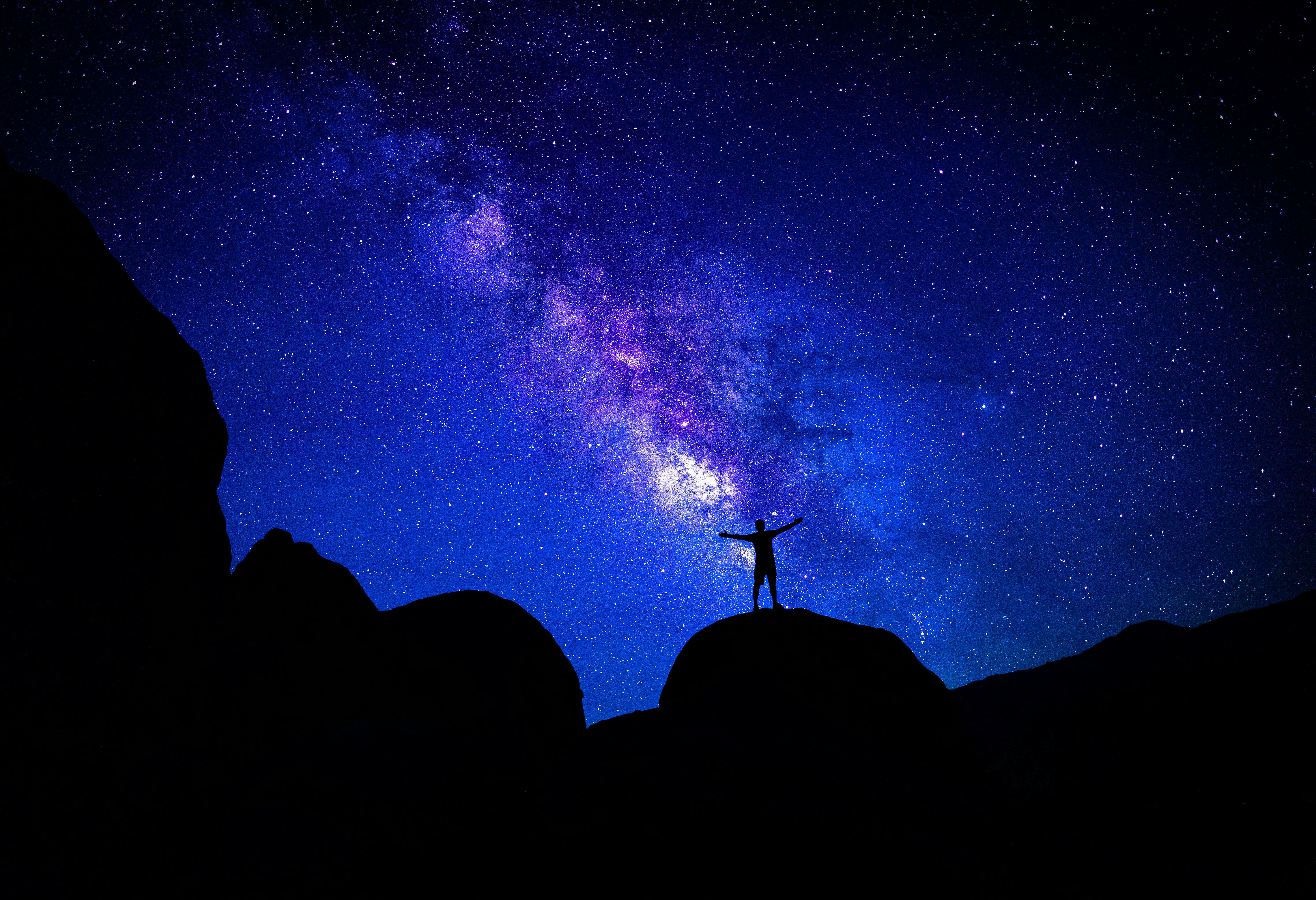 A silhouette of a person standing on a mountain ridge, looking up at a star-filled night sky